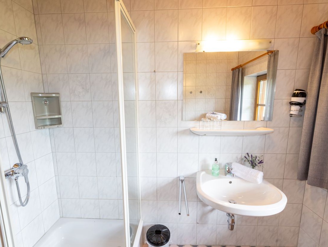 Helles Badezimmer mit Dusche, Waschbecken und Spiegel auf weiß gefliesten Wänden