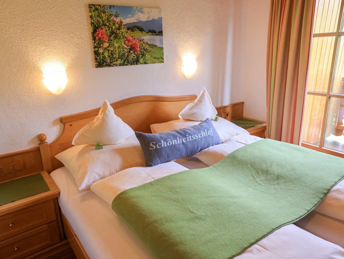 Doppelbett mit grünem Überwurf, Wandbild und Nachttischen in einem hellen Zimmer