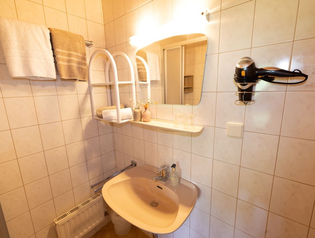 adezimmer mit Waschbecken, Spiegel, Handtuchhalter und Föhn an der Wand