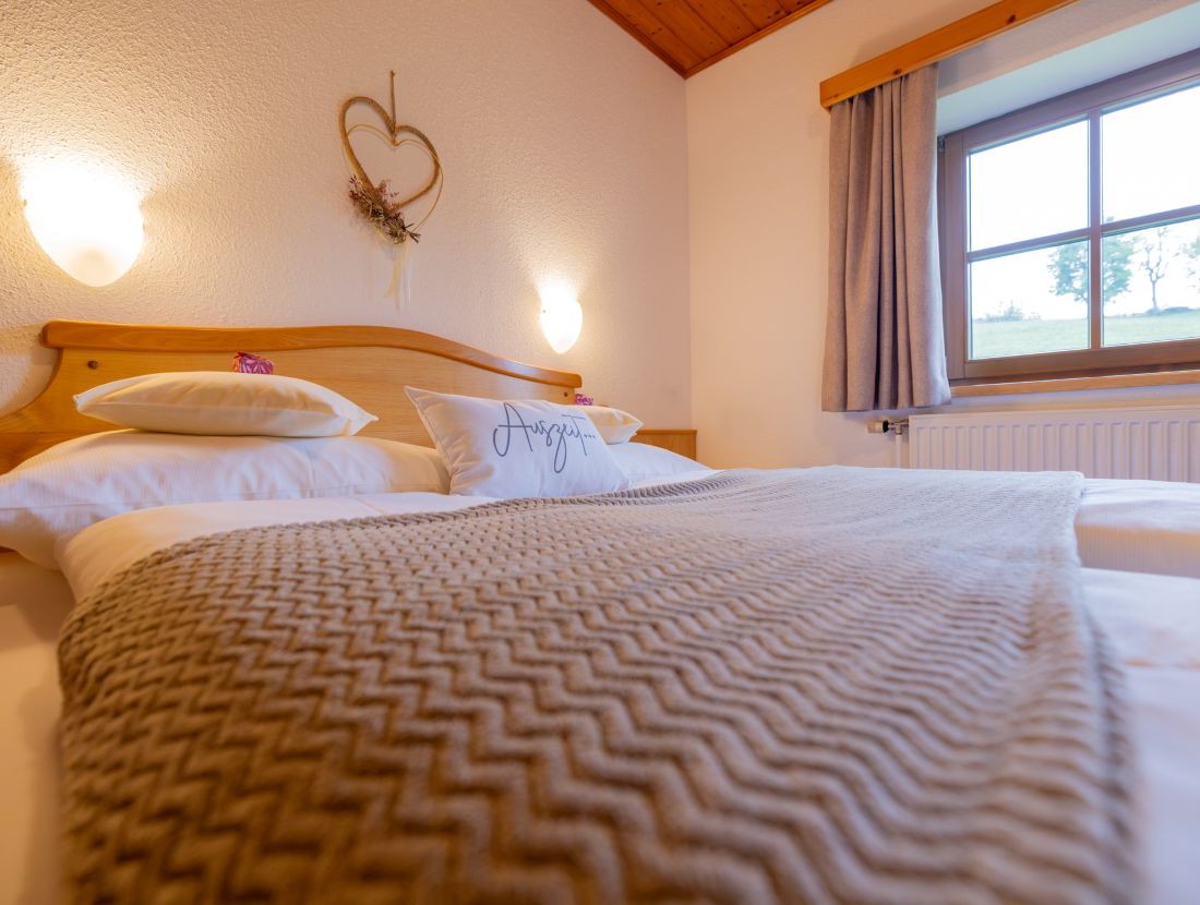 Gemütliches Schlafzimmer mit Doppelbett, dekoriertem Herz an der Wand und Fensterblick