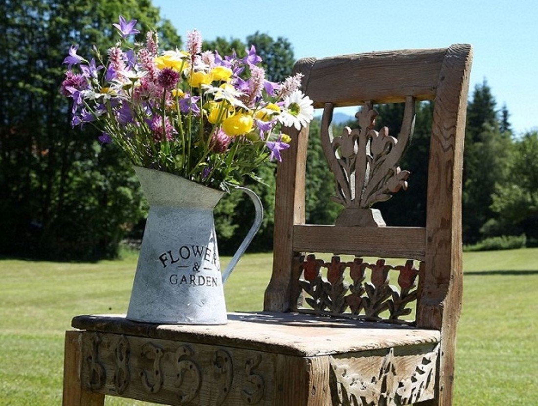 Ein Krug mit bunten Blumen steht auf einem kunstvoll verzierten Holzstuhl im Freien
